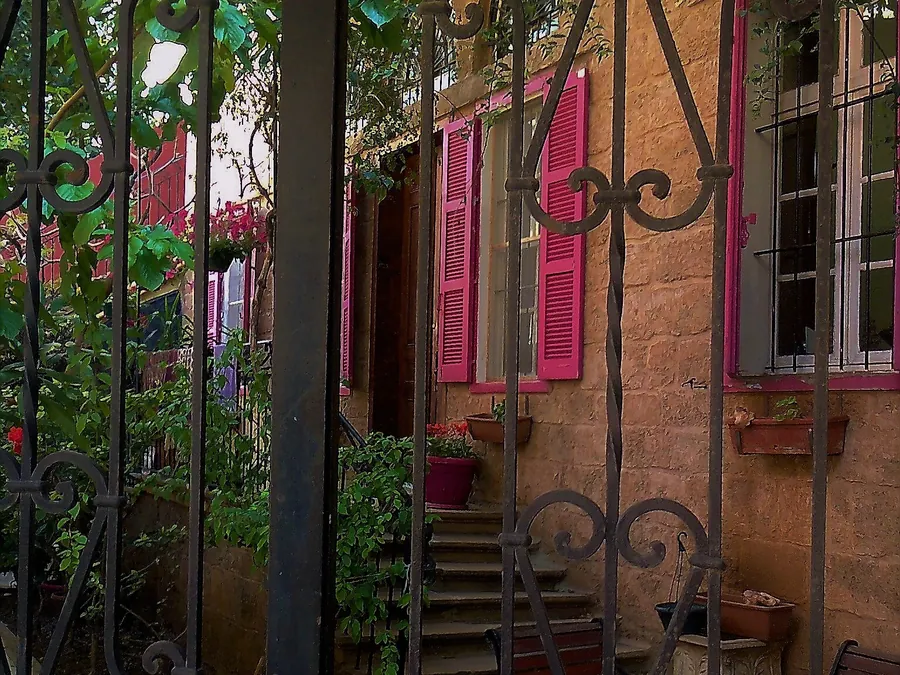 An iron gate opening onto a garden staircase and pink shutters in Achrafieh